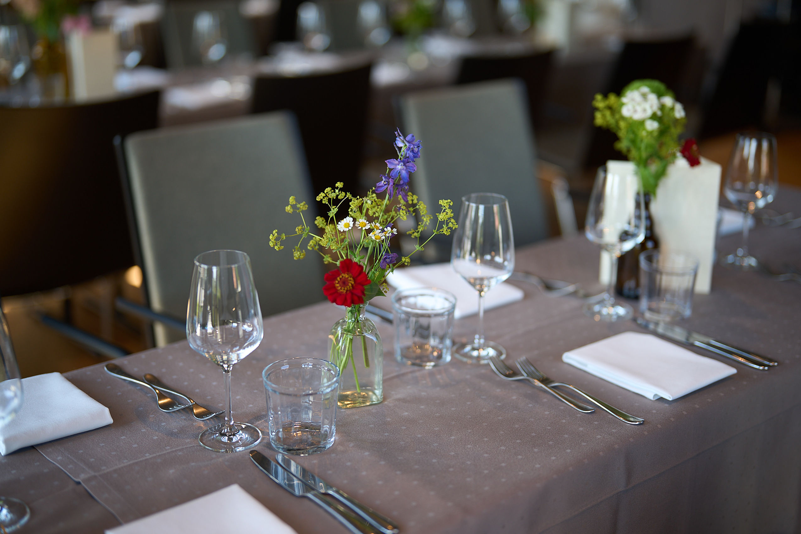 Eine kleine Vase mit bunten Blumen und verschiedenen Gläsern auf einem Tisch im Eventsaal des Hotel FREIgeist in Göttingen Nordstadt