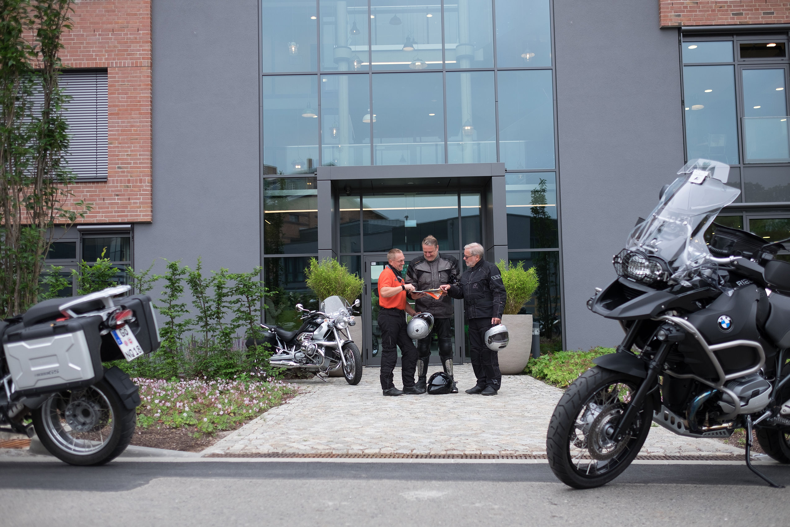 Drei Herren mit Motorradkleidung stehen am Eingang vor dem Biker Hotel im Harz und schauen auf eine Karte