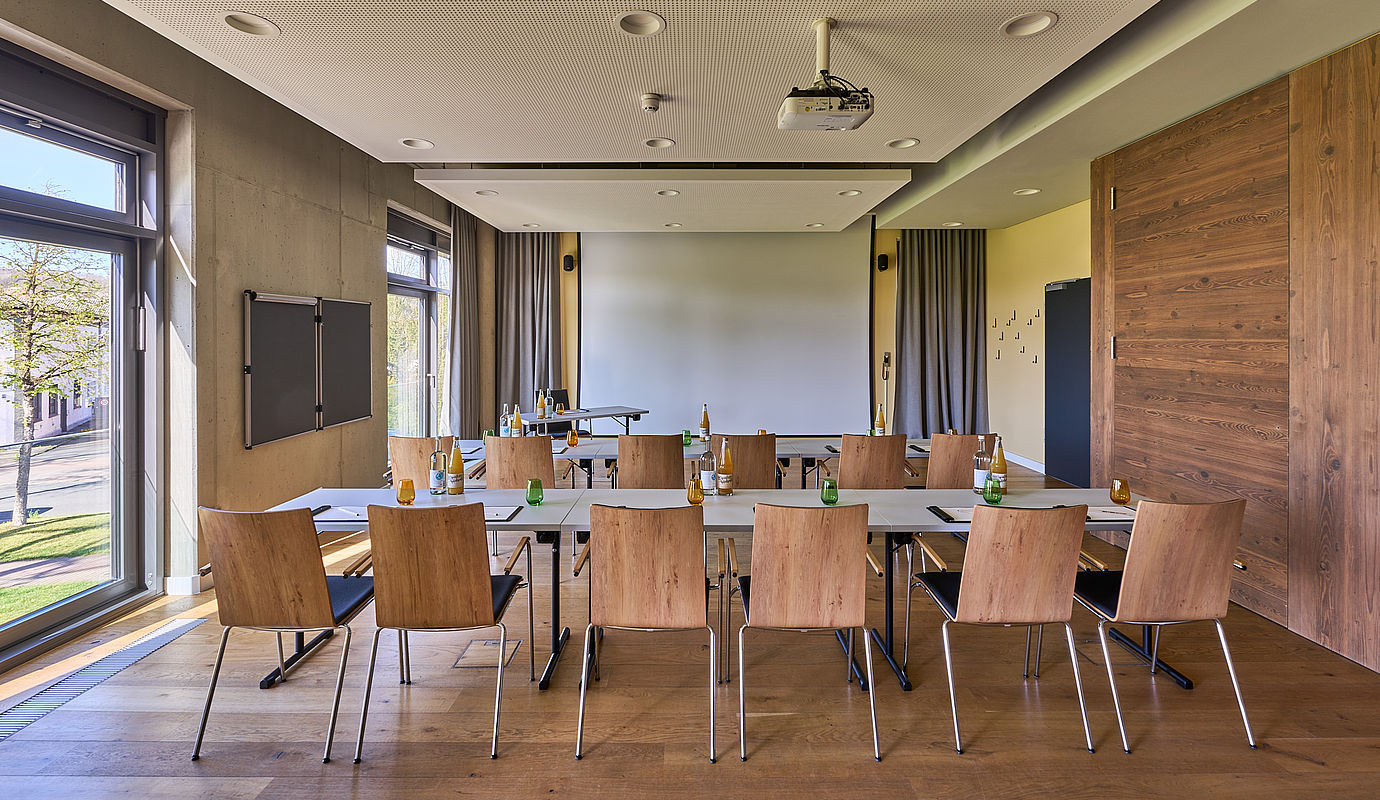 Holzstühle um einen Tisch mit Blick auf einen Projektionsschirm in einem Konferenzraum