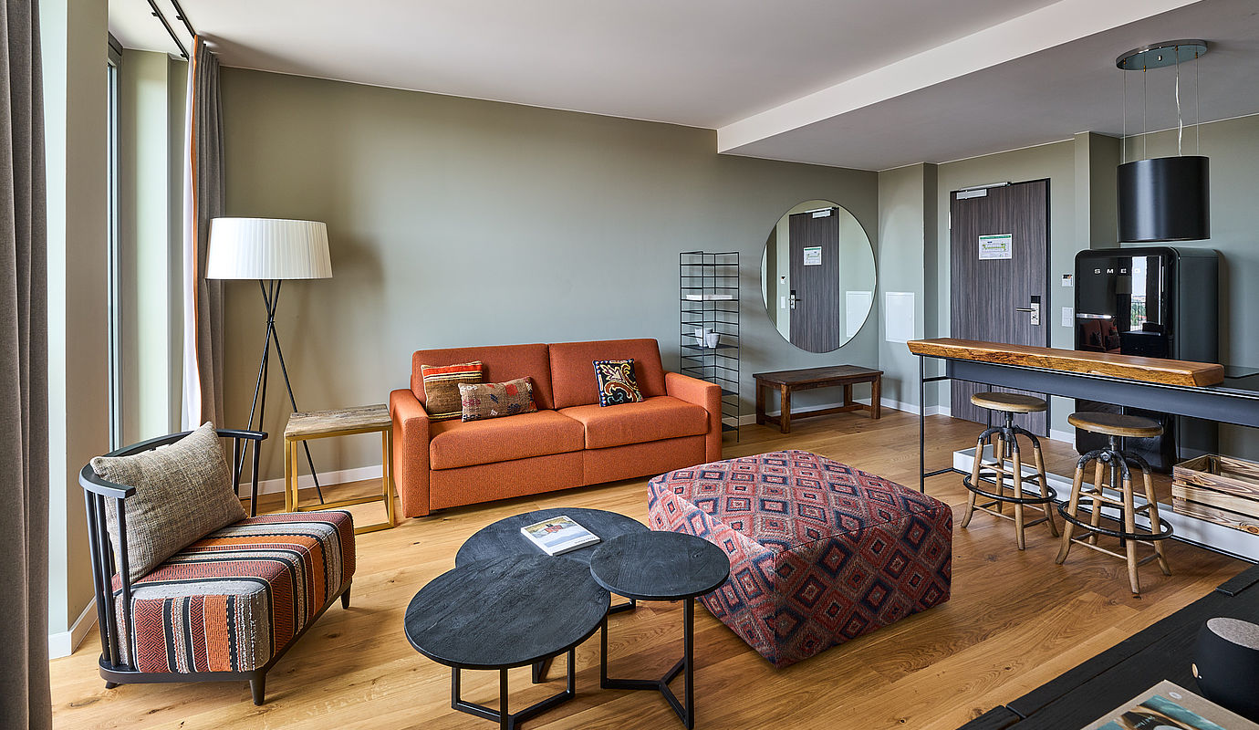 Das weite Apartment des Hotel FREIgeist mit einem orangenen Sofa und einer kleinen Truhe