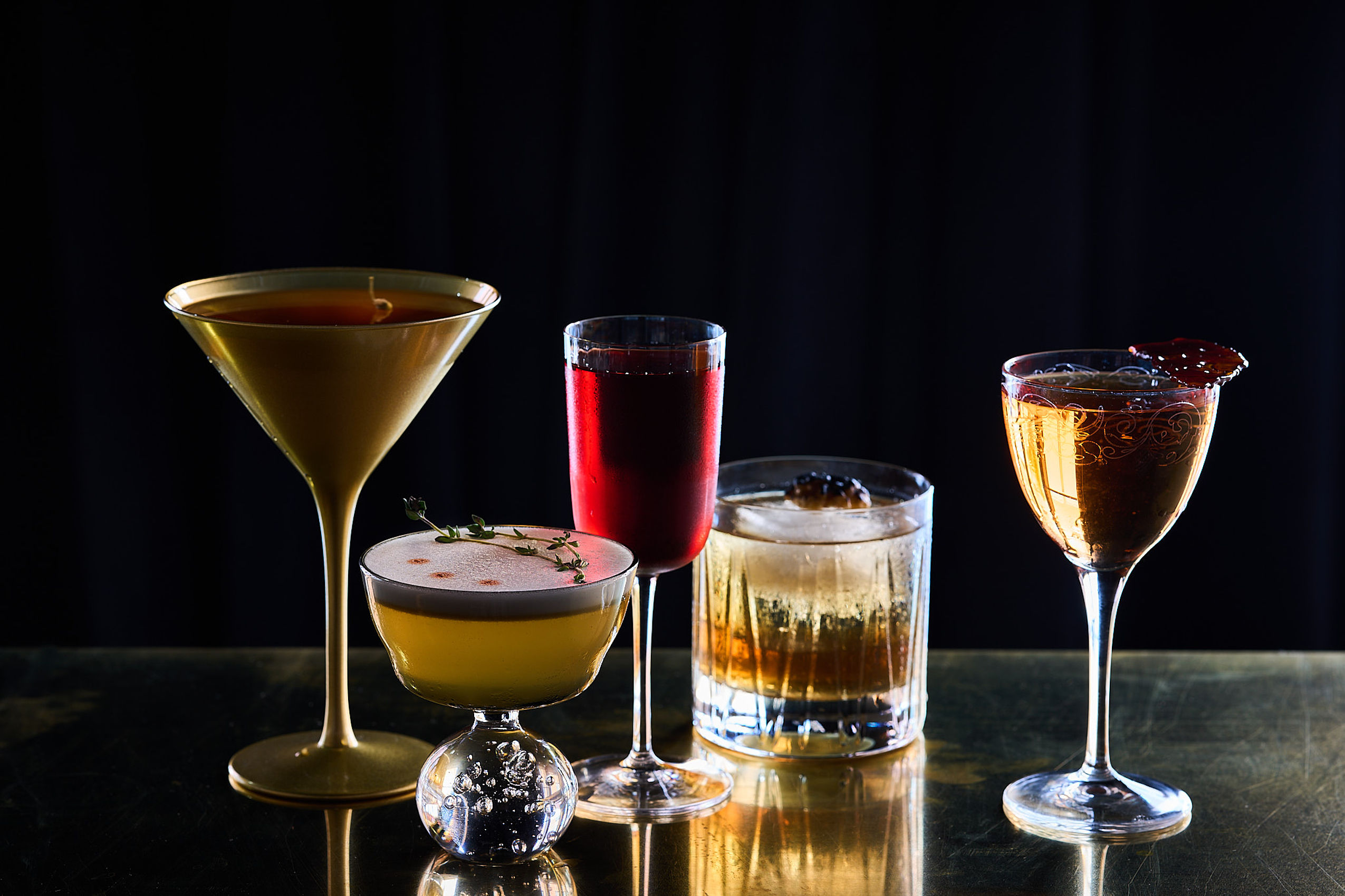 Mehrere Cocktails und Drinks in verschiedenen Gläsern stehen auf einem beleuchteten Tisch