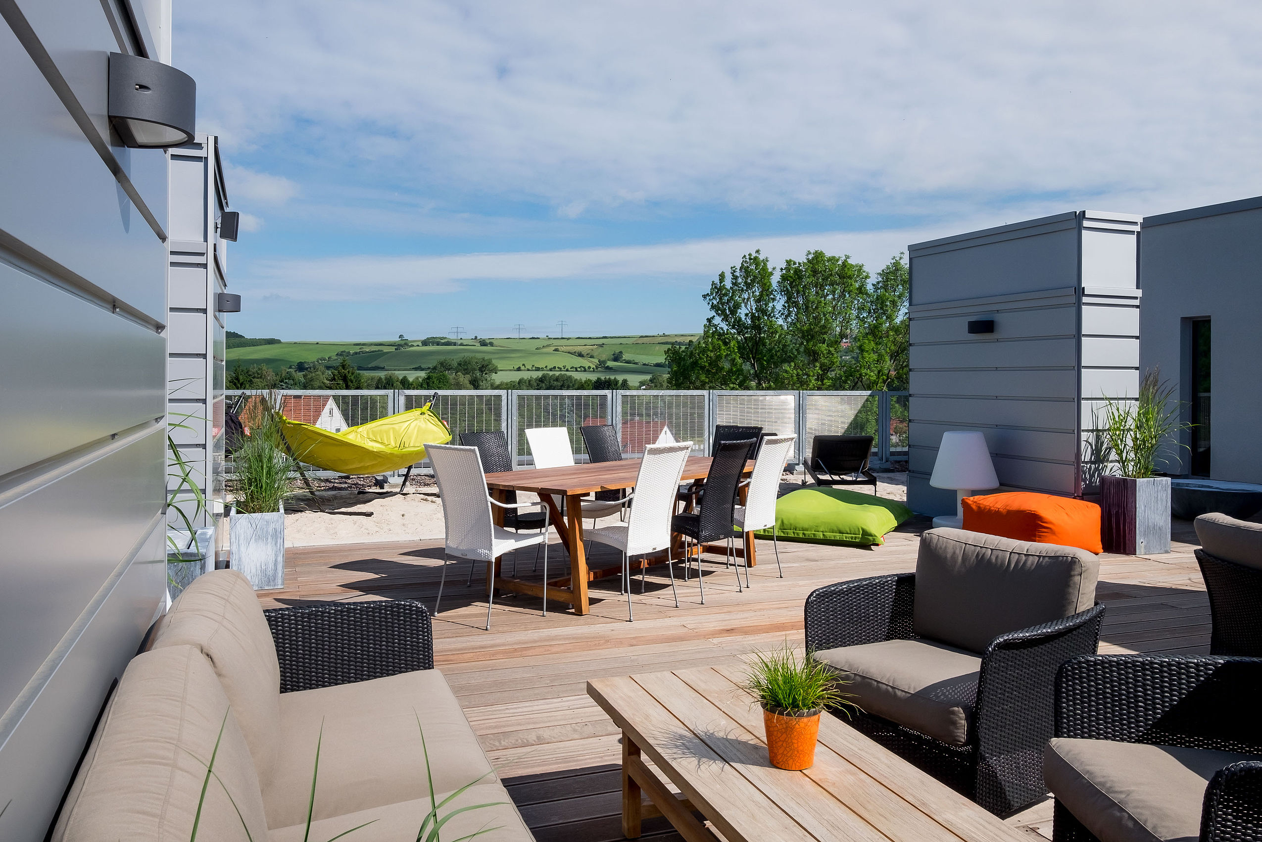 Auf einer Dachterrasse im Design Hotel Hannover steht ein großer Holztisch, Terrassenmöbel und eine grüne Hängematte