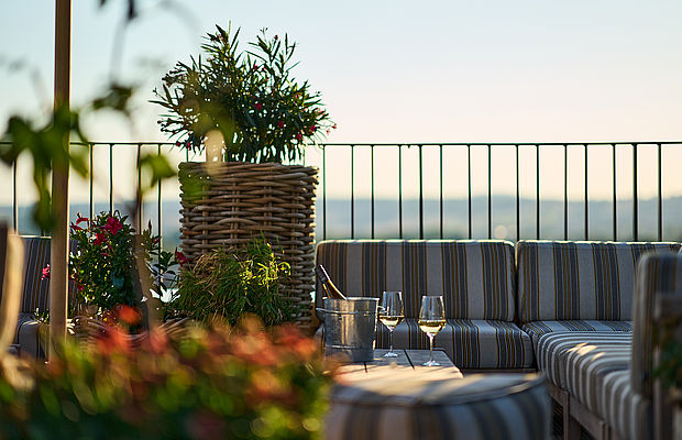 Gemütliches Sofa, Tisch mit zwei Gläsern Sekt und Pflanzen auf der Terrasse der Skybar