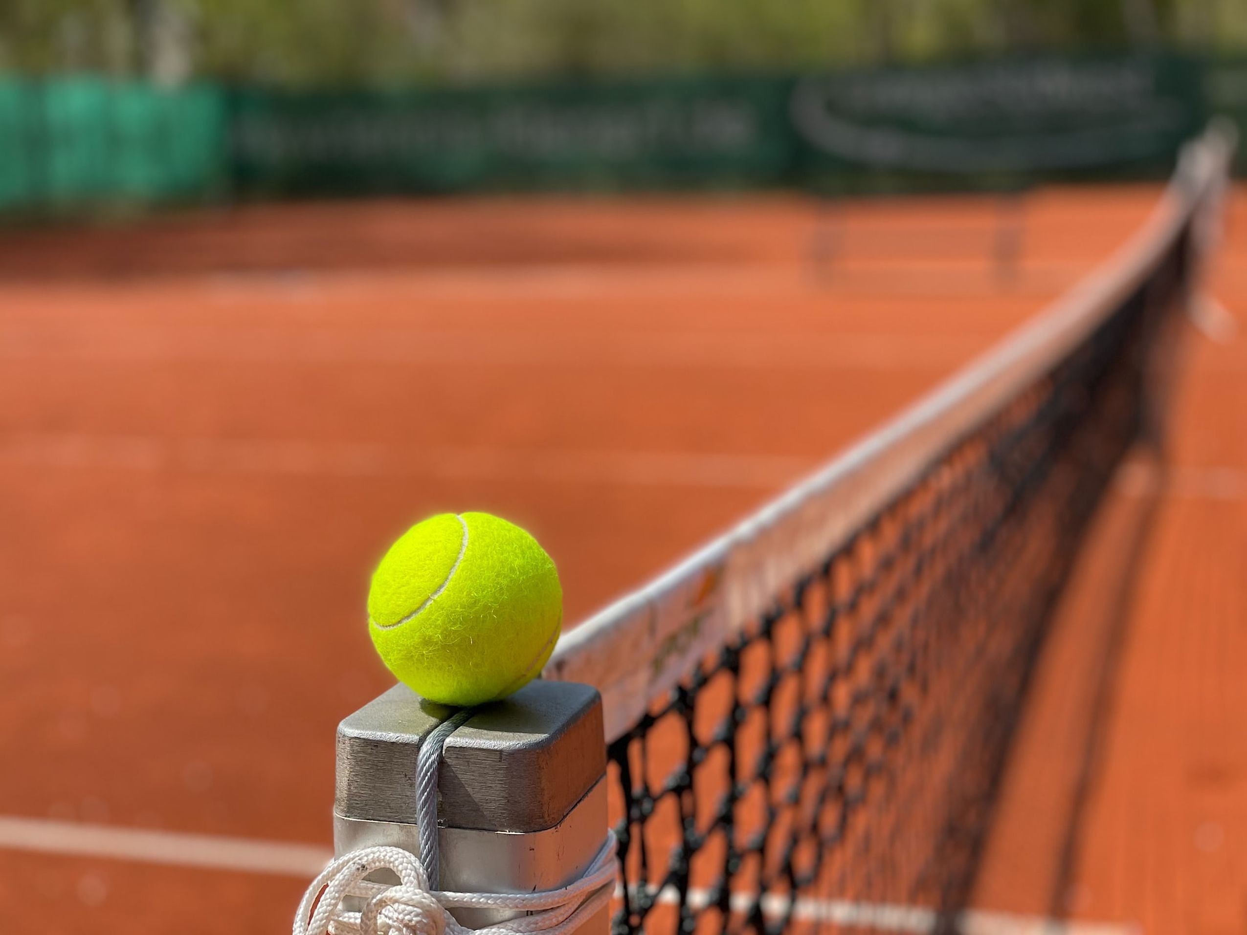 Detailaufnahme eines gelben Tennisballs der auf dem Pfosten des Netztes liegt