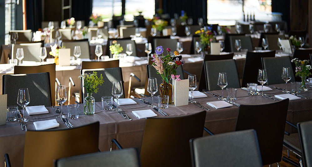Veranstaltungssaal mit festlich gedeckten Tischen und bunten Blumensträußen.