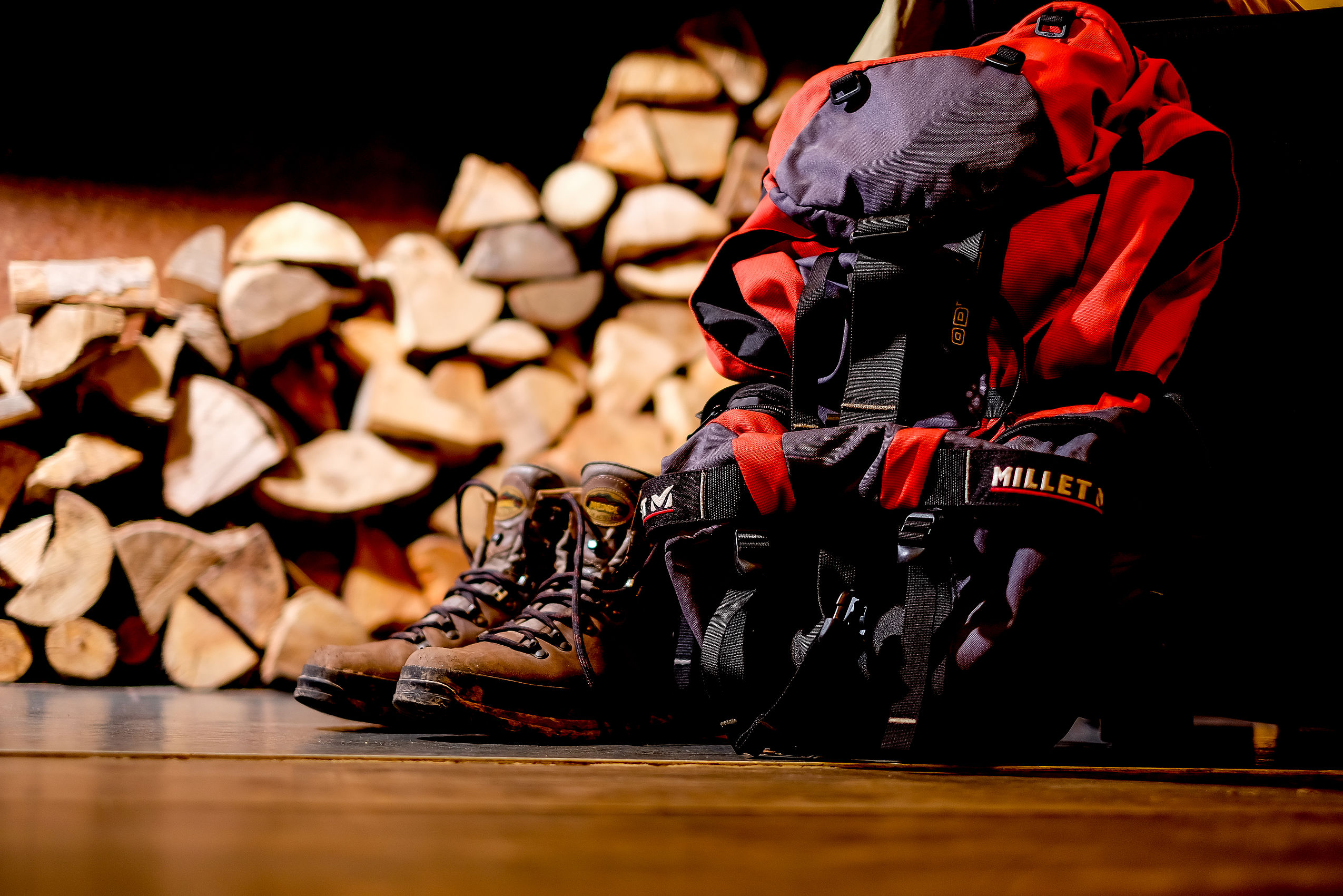 Ein Paar Wanderstiefel und ein Rucksack stehen vor mehreren Holzscheiten für einen Wanderurlaub im Harz