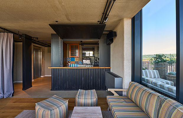Eine Bar und eine gestreifte blaue und beige Sitzecke neben einem Fenster der Skybar