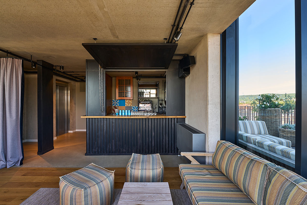 Eine Bar und eine gestreifte blaue und beige Sitzecke neben einem Fenster der Skybar