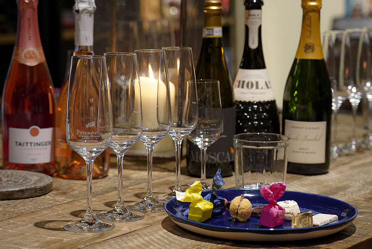 Champagnerflaschen, Dolci und Sektgläser aneinandergereiht auf einem Holzregal
