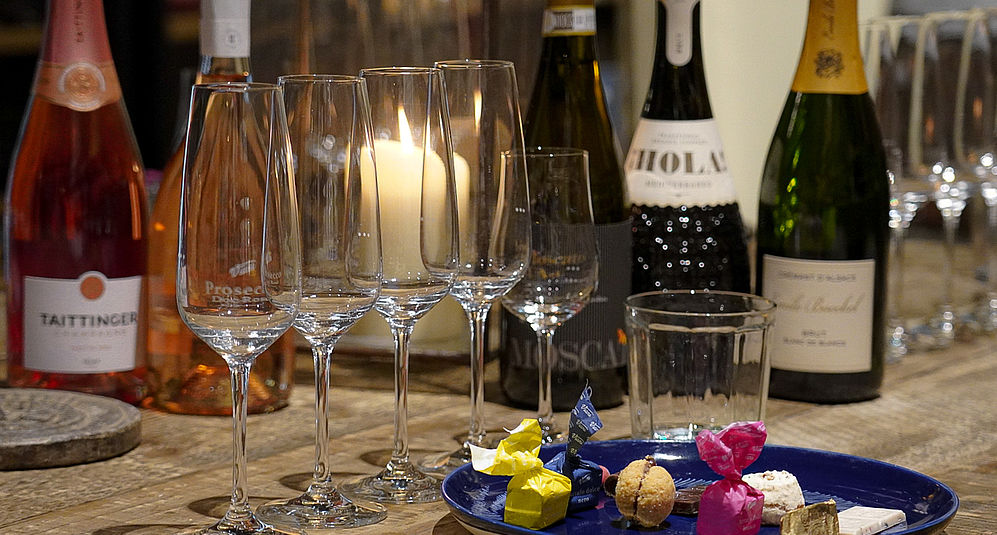 Champagnerflaschen, Dolci und Sektgläser aneinandergereiht auf einem Holzregal