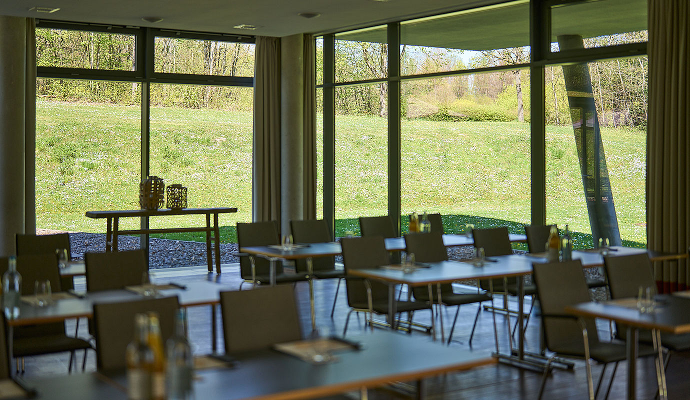 Aufgestellte Tische und Stühle im Konferenzraum mit großen Panoramafenstern mit Blick in den Garten