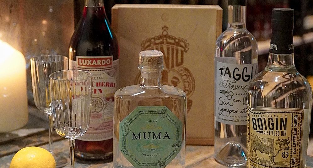 Verschiedene Gin-Sorten des Viani Alimentari auf einem Holztisch neben einer Kerze 