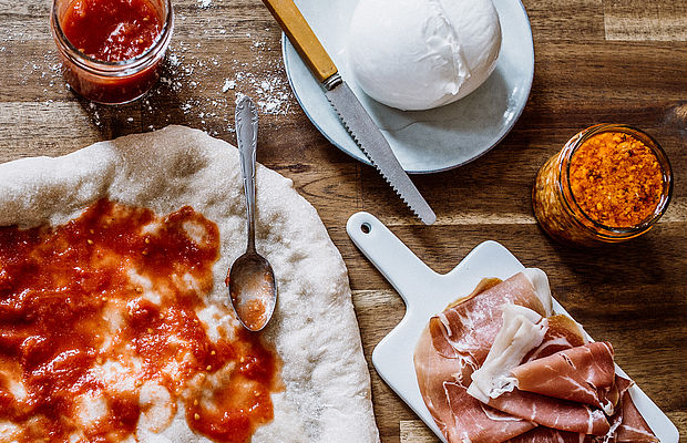 Eine Pizza mit Tomatensoße, mit Pesto, Burrata und Schinken nebenstehend