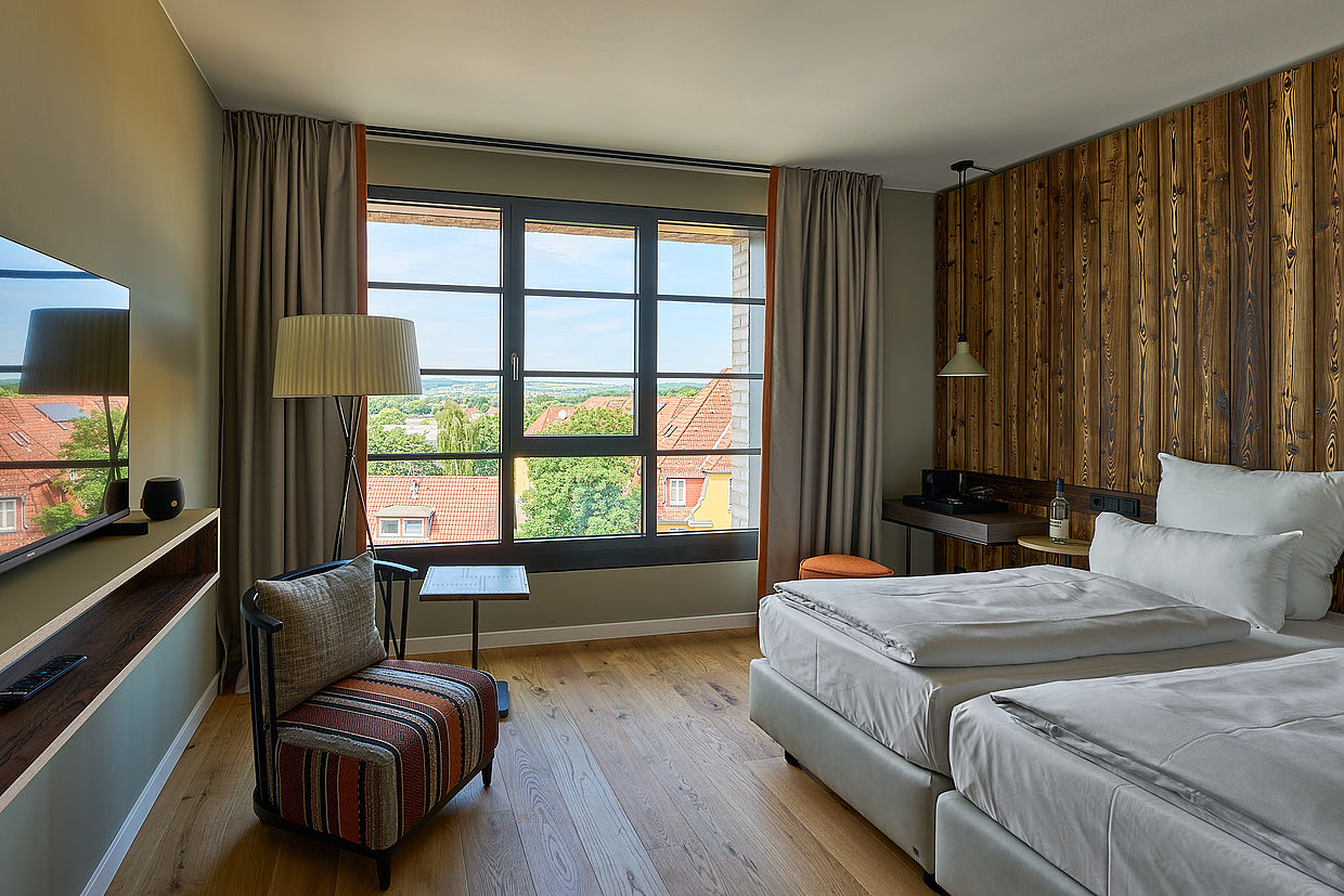 Blick auf ein helles Hotelzimmer mit großem Fenster und schönem Holzboden