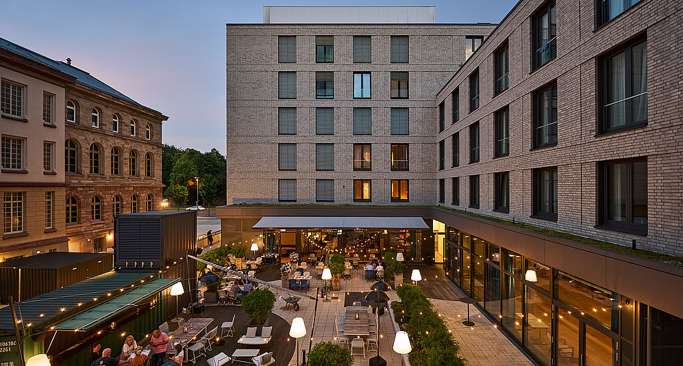 Abendszene im Innenhof des Hotels mit Terrasse, Licht und Gästen.