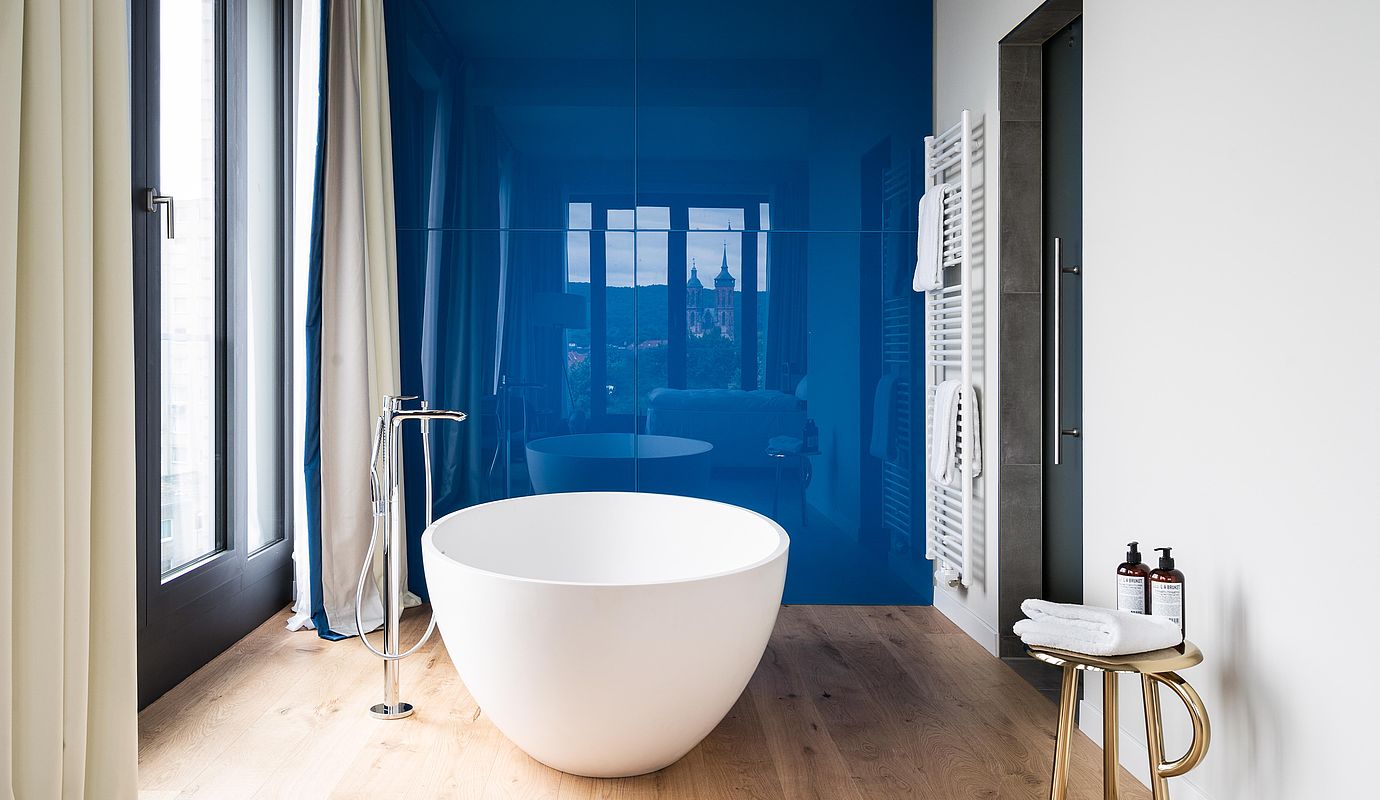 Eine runde, freistehende Badewanne vor einer blau glänzenden Wand