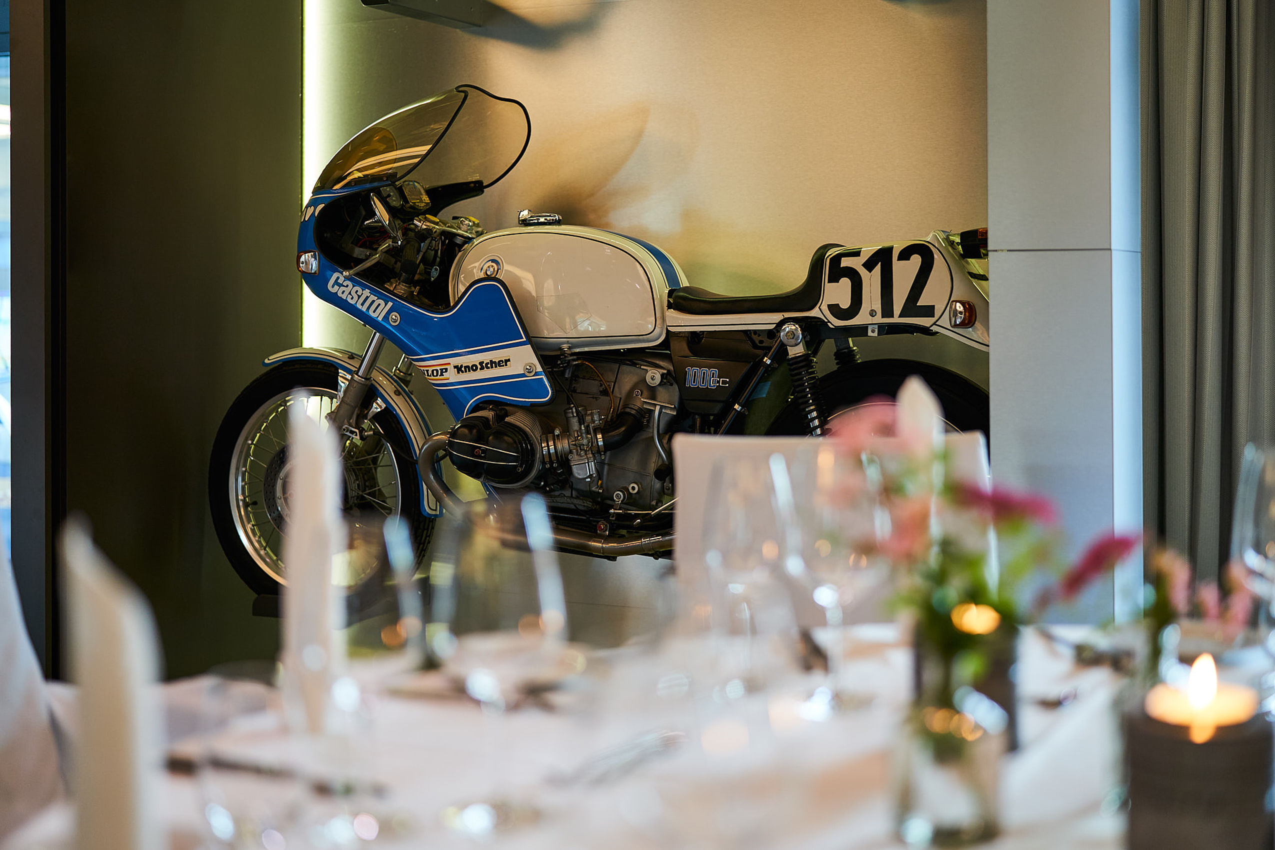 Fokusaufnahme auf ein blaues Motorrad mit der Nummer 512 und der eingedeckte Tisch im Vordergrund ist unscharf