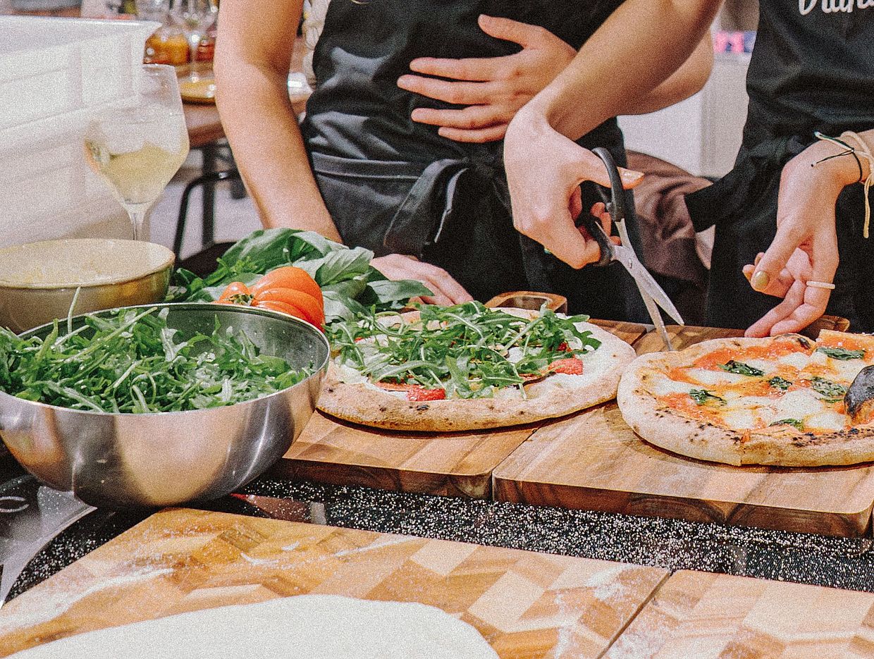 Zwei Personen in Viani-Schürzen schneiden eine Pizza an einem Tisch mit drei Pizzen.